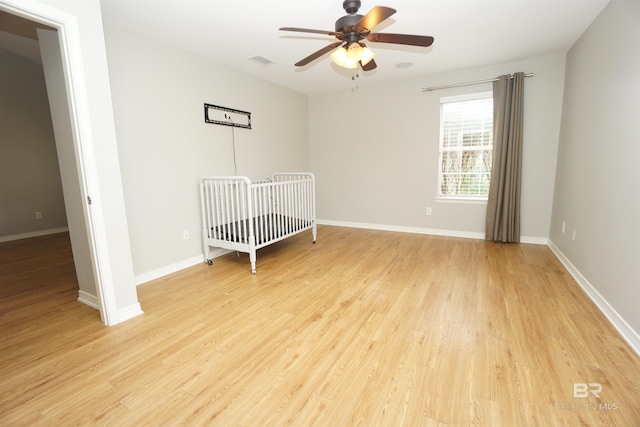 unfurnished bedroom featuring ceiling fan, a nursery area, and light wood-type flooring