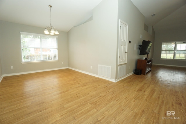 empty room with an inviting chandelier, vaulted ceiling, and light hardwood / wood-style flooring