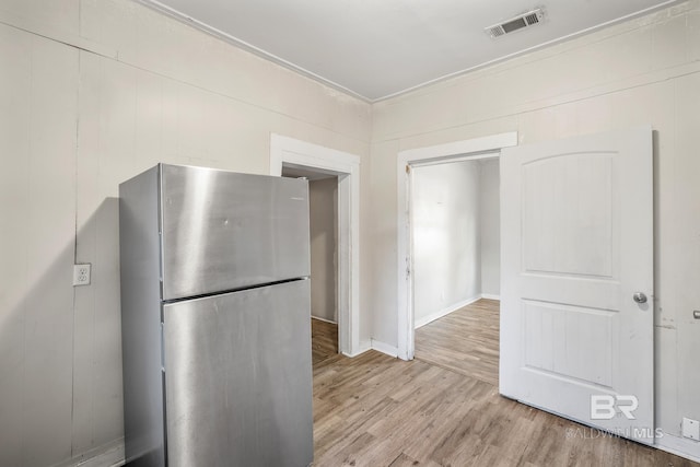 kitchen with light wood-type flooring, wooden walls, crown molding, and stainless steel refrigerator