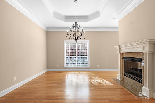 unfurnished living room with a tray ceiling, crown molding, light hardwood / wood-style floors, and an inviting chandelier