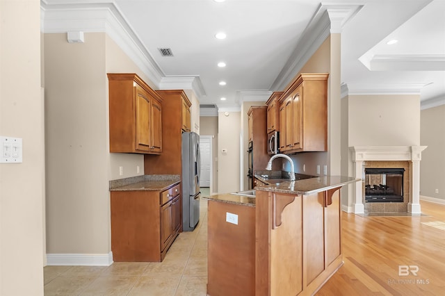 kitchen featuring stainless steel appliances, a kitchen breakfast bar, crown molding, dark stone counters, and light wood-type flooring