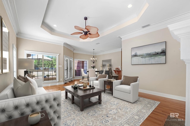 living room with ceiling fan with notable chandelier, light wood-type flooring, a tray ceiling, and ornamental molding