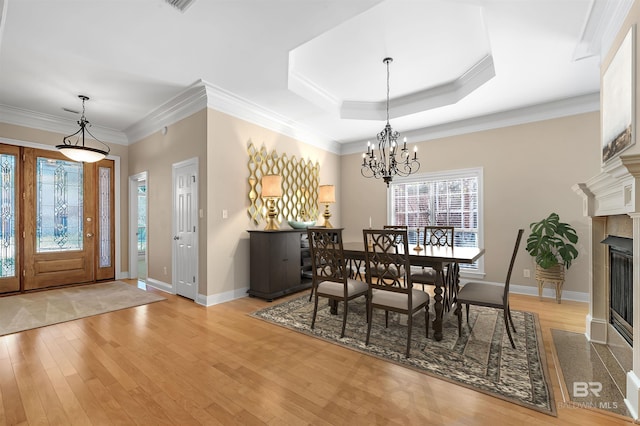 dining room with a tray ceiling, light hardwood / wood-style flooring, a chandelier, and ornamental molding