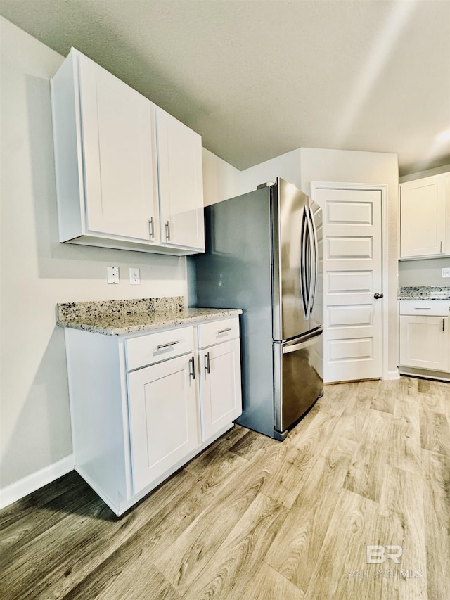 kitchen with light stone countertops, light wood-type flooring, white cabinets, and stainless steel refrigerator