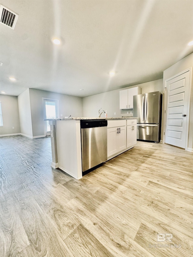 kitchen with light hardwood / wood-style flooring, stainless steel appliances, light stone countertops, an island with sink, and white cabinets