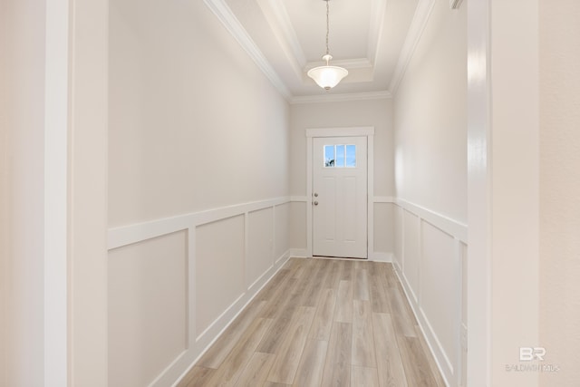 doorway featuring a raised ceiling, a decorative wall, ornamental molding, wainscoting, and light wood-type flooring