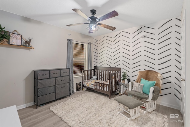 bedroom featuring a crib, ceiling fan, and light hardwood / wood-style floors