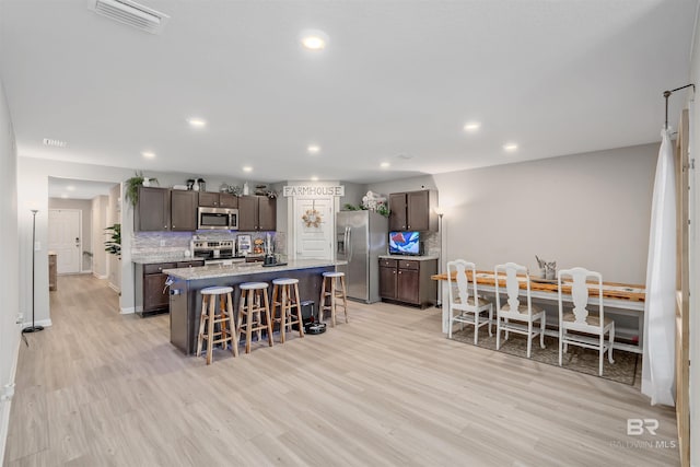 kitchen with stainless steel appliances, light wood-type flooring, backsplash, a breakfast bar area, and a kitchen island with sink