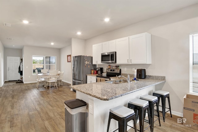 kitchen with stainless steel appliances, sink, white cabinetry, kitchen peninsula, and light stone countertops