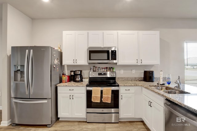 kitchen with appliances with stainless steel finishes, light stone countertops, white cabinets, light hardwood / wood-style flooring, and sink