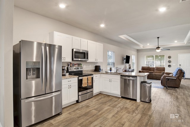 kitchen with a raised ceiling, white cabinetry, kitchen peninsula, and appliances with stainless steel finishes