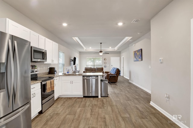 kitchen featuring kitchen peninsula, a tray ceiling, white cabinets, appliances with stainless steel finishes, and ceiling fan