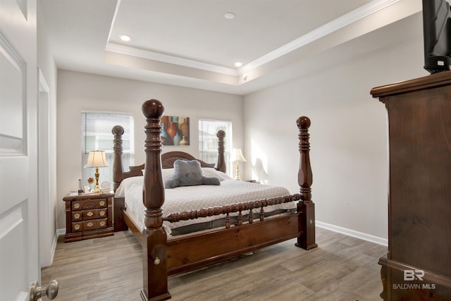 bedroom with light wood-type flooring, multiple windows, and a tray ceiling