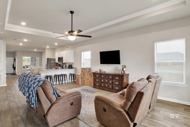 living room with ceiling fan, a tray ceiling, crown molding, and light hardwood / wood-style floors