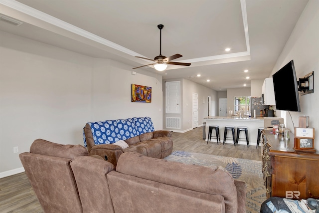 living room with light hardwood / wood-style floors, ceiling fan, and a raised ceiling