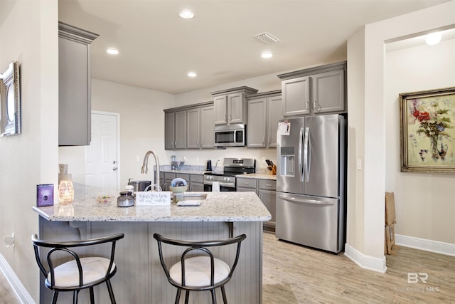 kitchen with a kitchen bar, kitchen peninsula, light stone counters, and stainless steel appliances