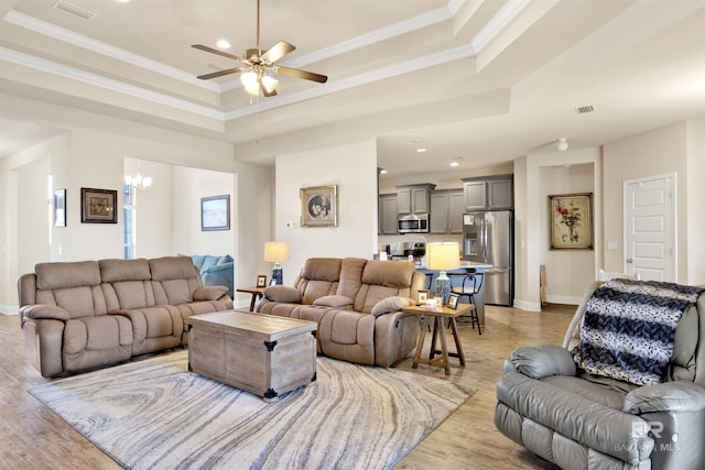 living room featuring a raised ceiling, crown molding, light hardwood / wood-style flooring, and ceiling fan