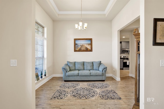 sitting room with a tray ceiling, crown molding, wood-type flooring, and a notable chandelier