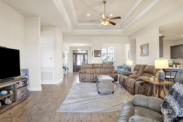 living room featuring ceiling fan with notable chandelier, a raised ceiling, crown molding, and light hardwood / wood-style flooring