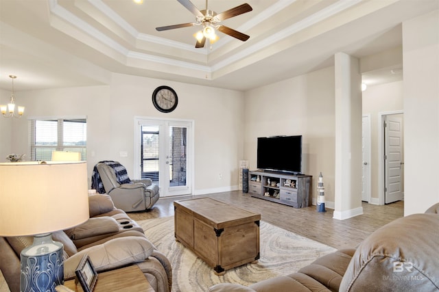 living room featuring french doors, ceiling fan with notable chandelier, crown molding, a tray ceiling, and light hardwood / wood-style floors