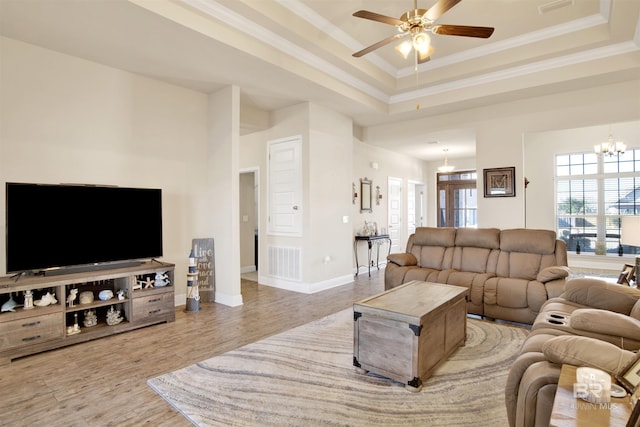 living room featuring ceiling fan with notable chandelier, a towering ceiling, ornamental molding, a tray ceiling, and wood-type flooring