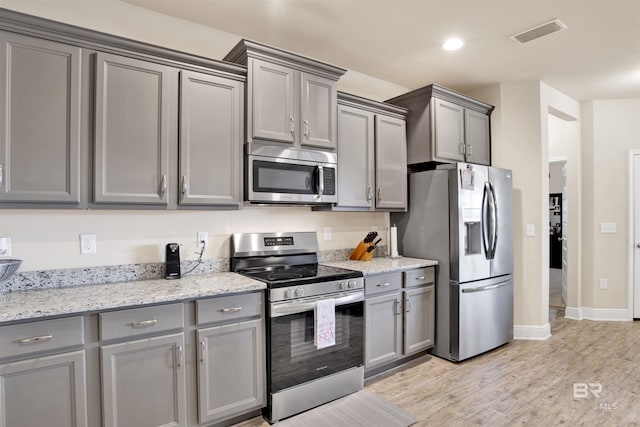 kitchen featuring stainless steel appliances, light hardwood / wood-style flooring, gray cabinetry, and light stone counters