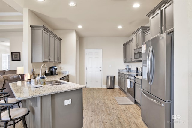 kitchen featuring a breakfast bar, sink, gray cabinets, light stone counters, and stainless steel appliances