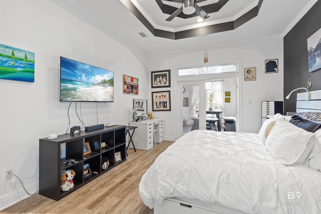 bedroom featuring light wood-type flooring, ceiling fan, a tray ceiling, and crown molding