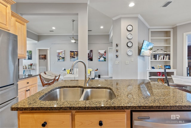 kitchen featuring stainless steel appliances, light brown cabinets, built in features, dark stone countertops, and sink