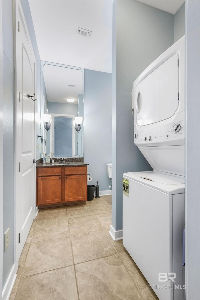 laundry area featuring visible vents, stacked washer and clothes dryer, a sink, baseboards, and laundry area