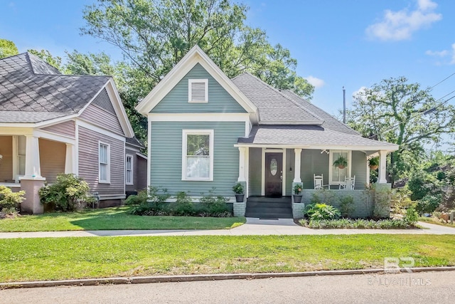 view of front of property featuring a porch, roof with shingles, and a front yard
