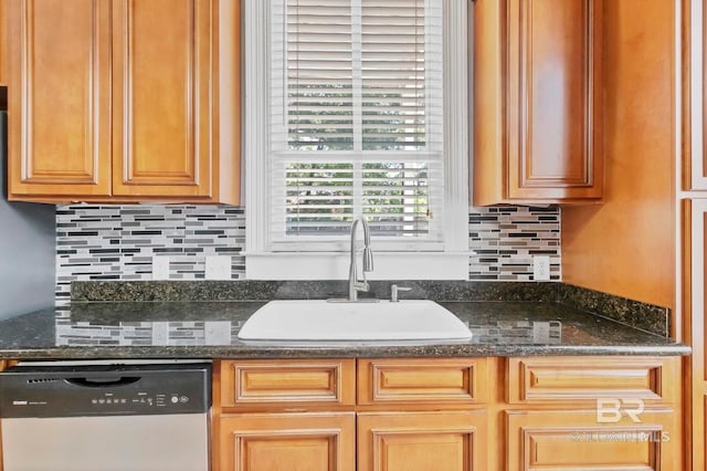 kitchen with a sink, dishwashing machine, dark stone counters, and backsplash