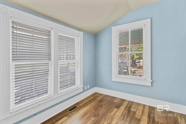 empty room featuring visible vents, baseboards, lofted ceiling, and wood finished floors