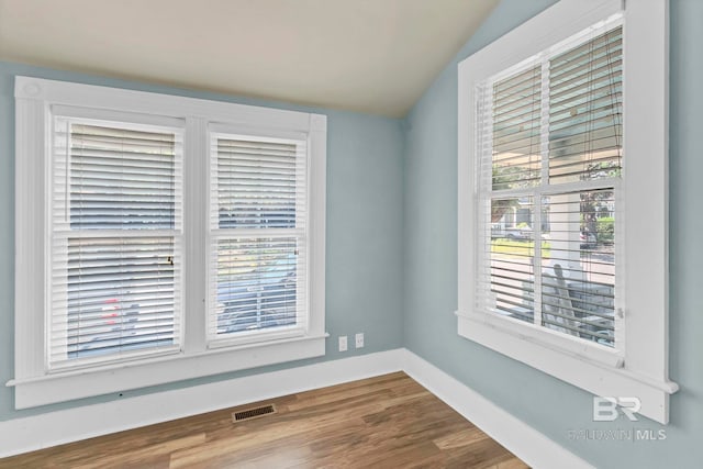 empty room featuring visible vents, baseboards, wood finished floors, and vaulted ceiling
