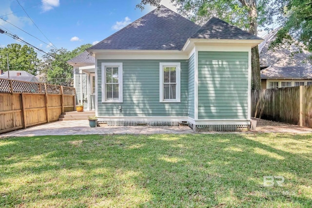 rear view of house with a fenced backyard, a shingled roof, a lawn, and a patio area