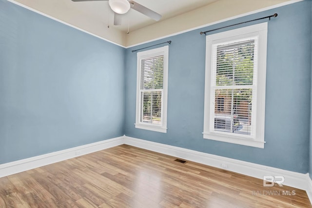 empty room with a ceiling fan, baseboards, a wealth of natural light, and wood finished floors