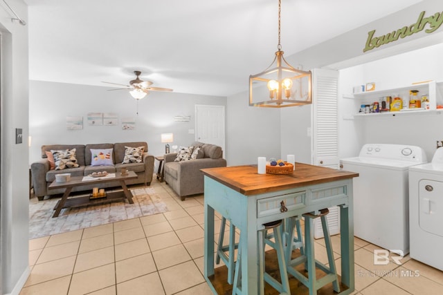 washroom with light tile patterned floors, washing machine and dryer, and ceiling fan with notable chandelier