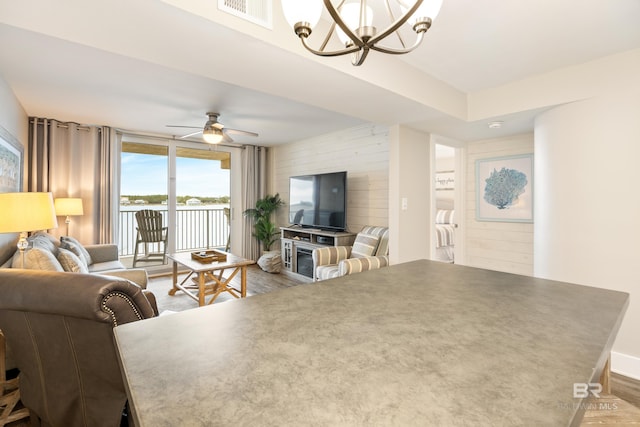 living room with ceiling fan with notable chandelier, wood finished floors, visible vents, and baseboards