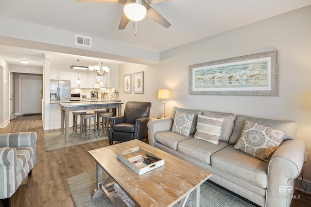 living area featuring visible vents, baseboards, ceiling fan with notable chandelier, wood finished floors, and ornate columns