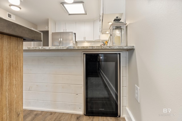 kitchen with light stone counters, beverage cooler, visible vents, white cabinets, and stainless steel fridge