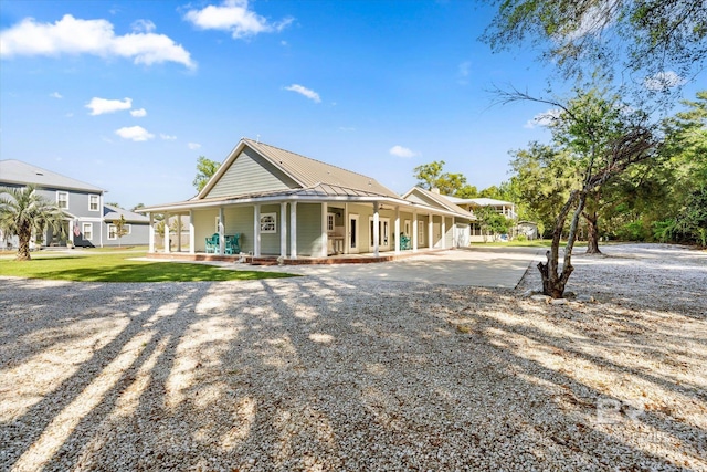 farmhouse with covered porch, a front yard, driveway, and metal roof
