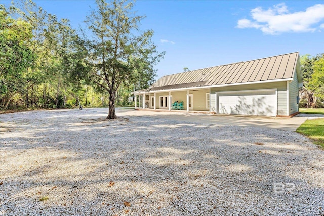 rear view of property with driveway, an attached garage, metal roof, and a standing seam roof