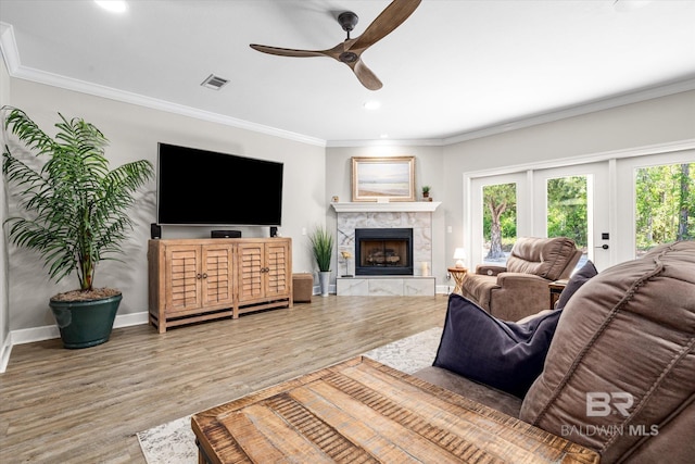 living room with crown molding, a fireplace, a ceiling fan, visible vents, and wood finished floors