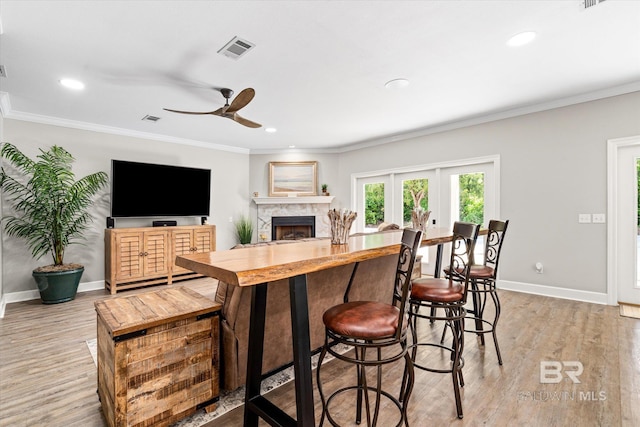 kitchen featuring baseboards, a stone fireplace, light wood-style flooring, visible vents, and ceiling fan