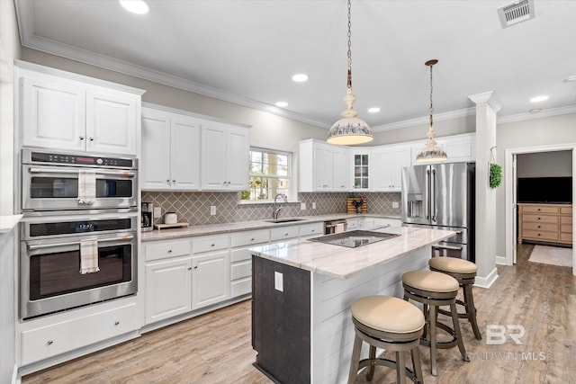kitchen featuring visible vents, a sink, a kitchen bar, stainless steel appliances, and backsplash