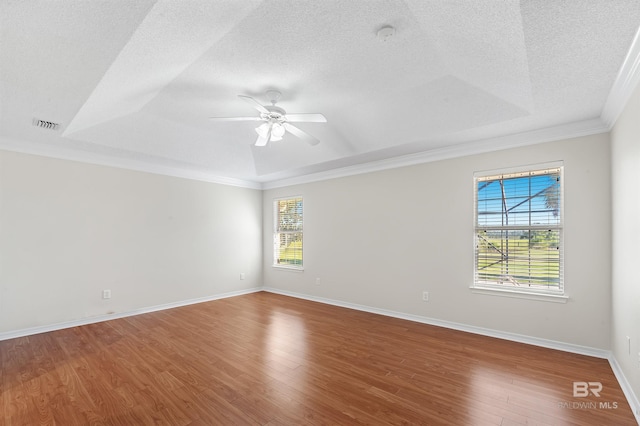 empty room featuring a textured ceiling, wood-type flooring, ornamental molding, a raised ceiling, and ceiling fan