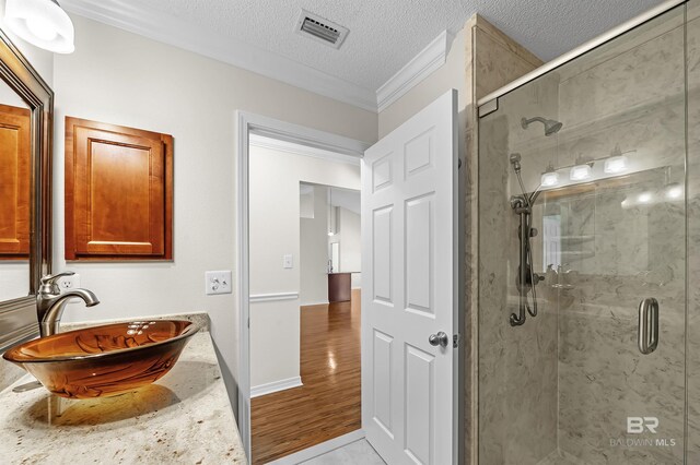 bathroom with a textured ceiling, tile patterned flooring, sink, ornamental molding, and a shower with shower door