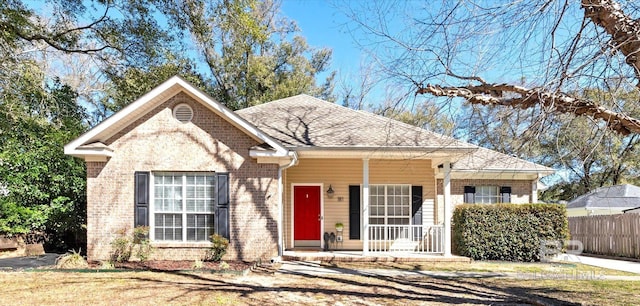 view of front of home featuring covered porch, brick siding, roof with shingles, and fence