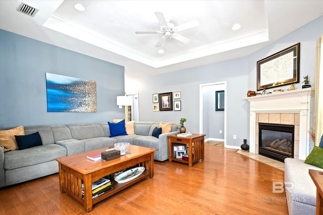 living area featuring light wood finished floors, a raised ceiling, visible vents, ornamental molding, and a tile fireplace