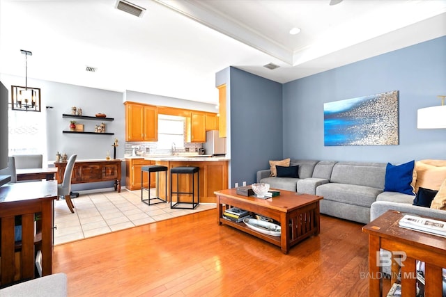 living area with light wood-style floors, a chandelier, a raised ceiling, and visible vents